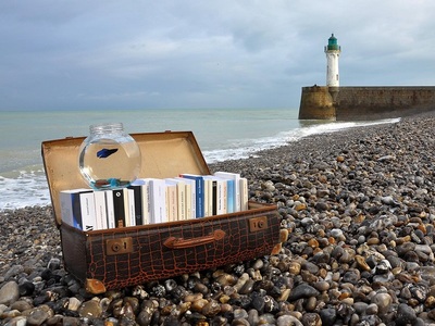Zdjęcie wprowadzające - otwarty kufer z książkami, plaża, kamienie, morze, latarnia morska